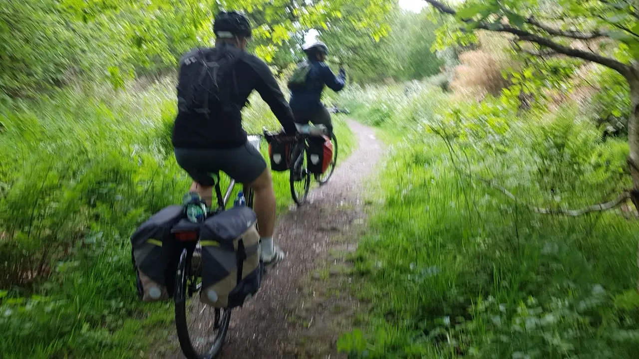 Two riders with panniers on a leafy path
