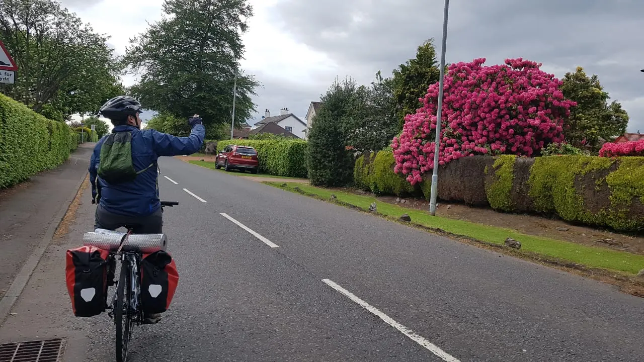 A rider with panniers waving on a quiet road