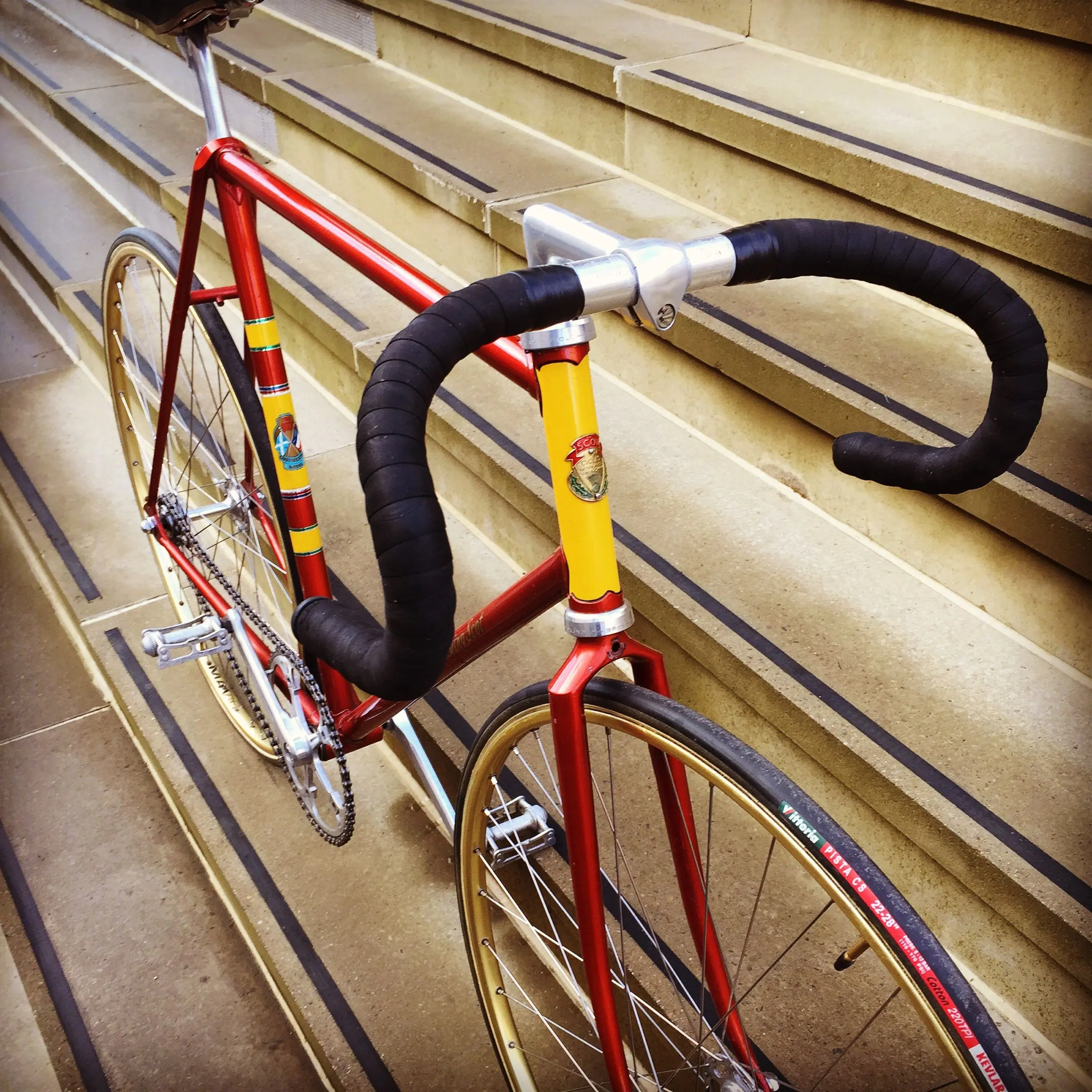 A red steel track bike with drop bars leaning against stone steps