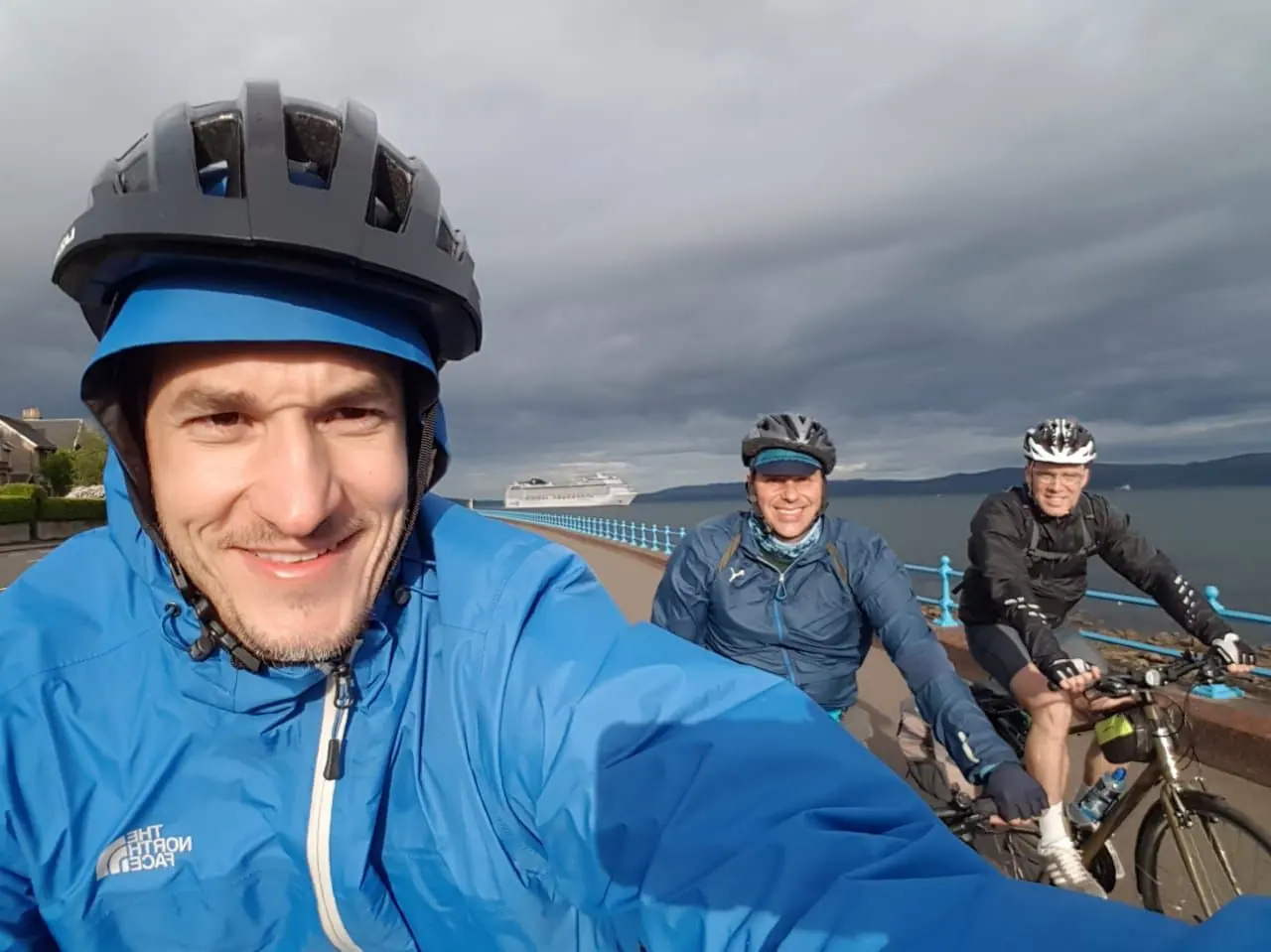 Three riders taking a selfie on a coastal road on a grey day