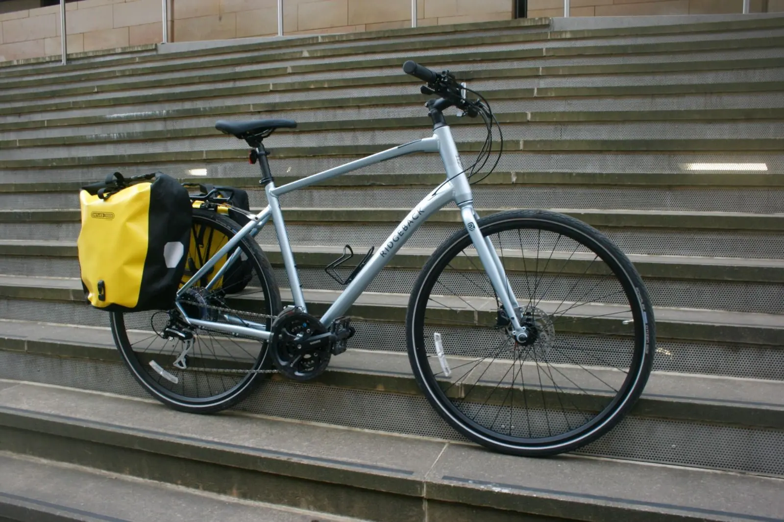A silver Ridgeback hire bike with a yellow Ortlieb pannier, parked on stone steps